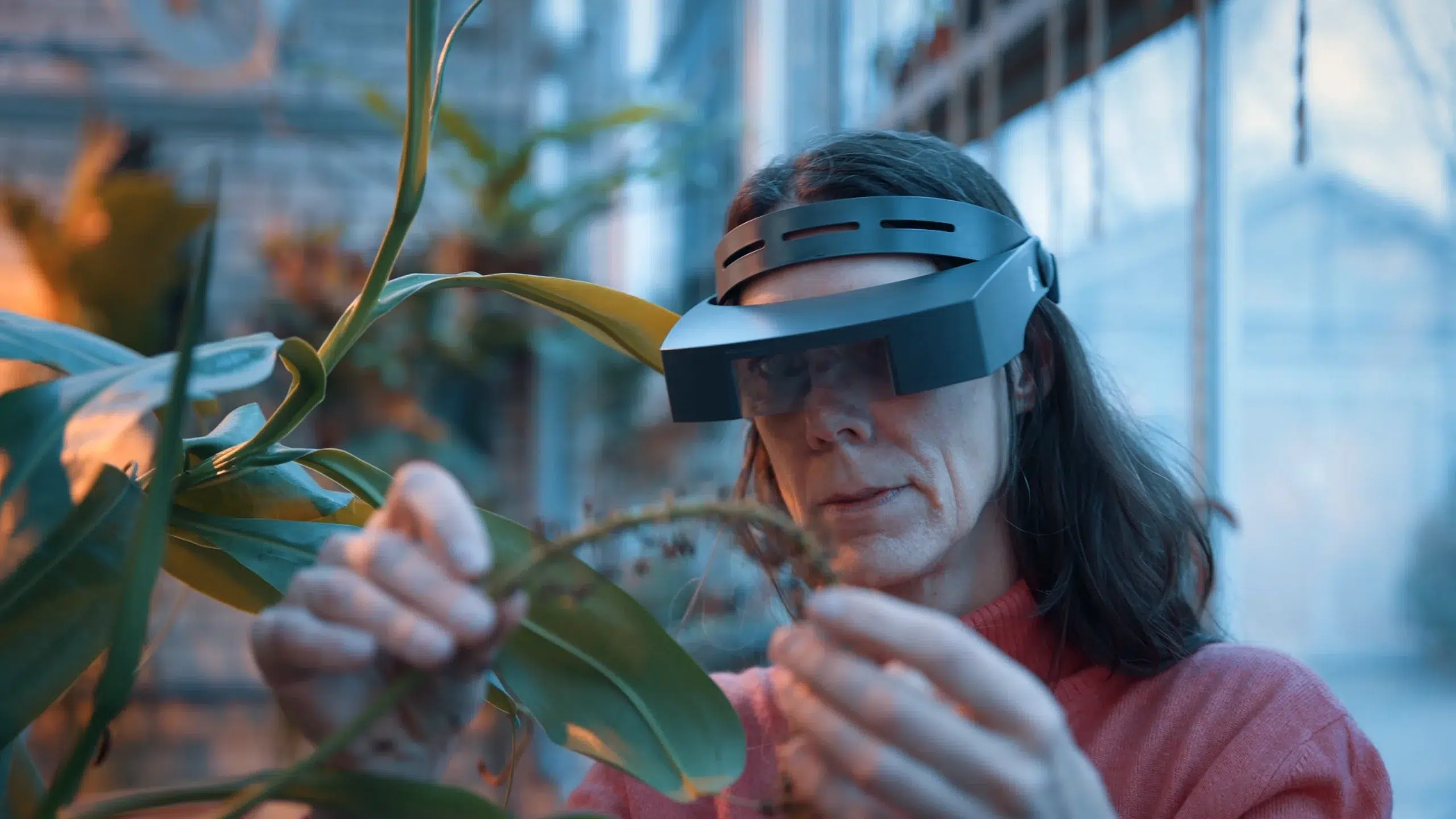 Botanikerin untersucht mit Augmented-Reality-Brille ein Pflanzenblatt im Gewächshaus — moderne Methoden der Pflanzenforschung