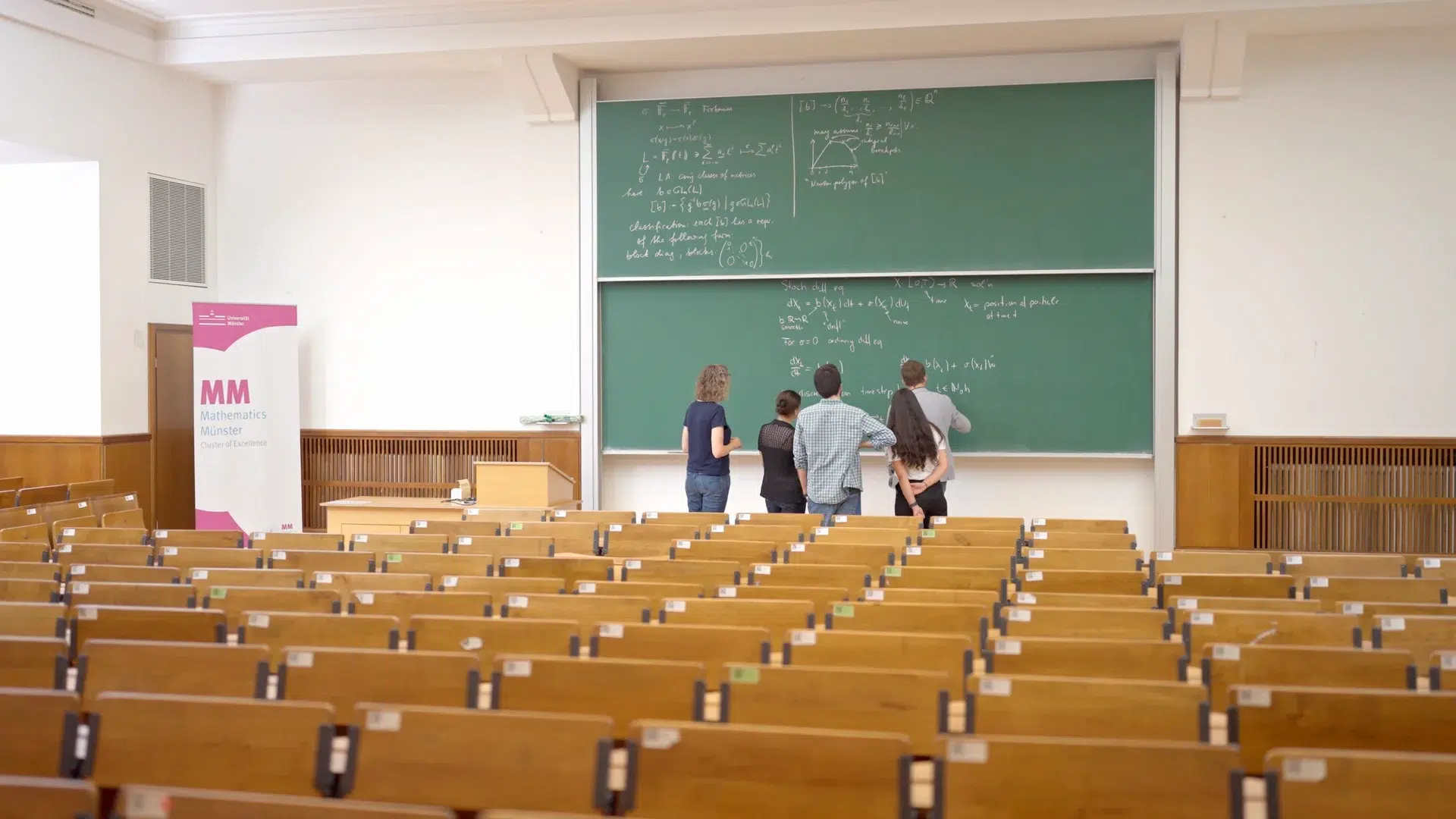 Vier Mathematiker*innen verschiedener Karrierestufen arbeiten gemeinsam an einer Tafel im Hörsaal des Exzellenzclusters Mathematik Münster