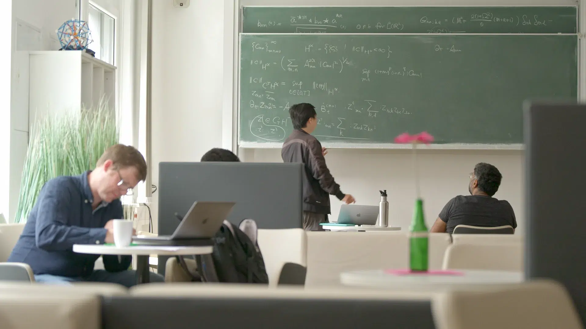 Co-Working-Lounge am Exzellenzcluster Mathematik Münster: Forschende arbeiten am Laptop und an der Tafel im Austausch